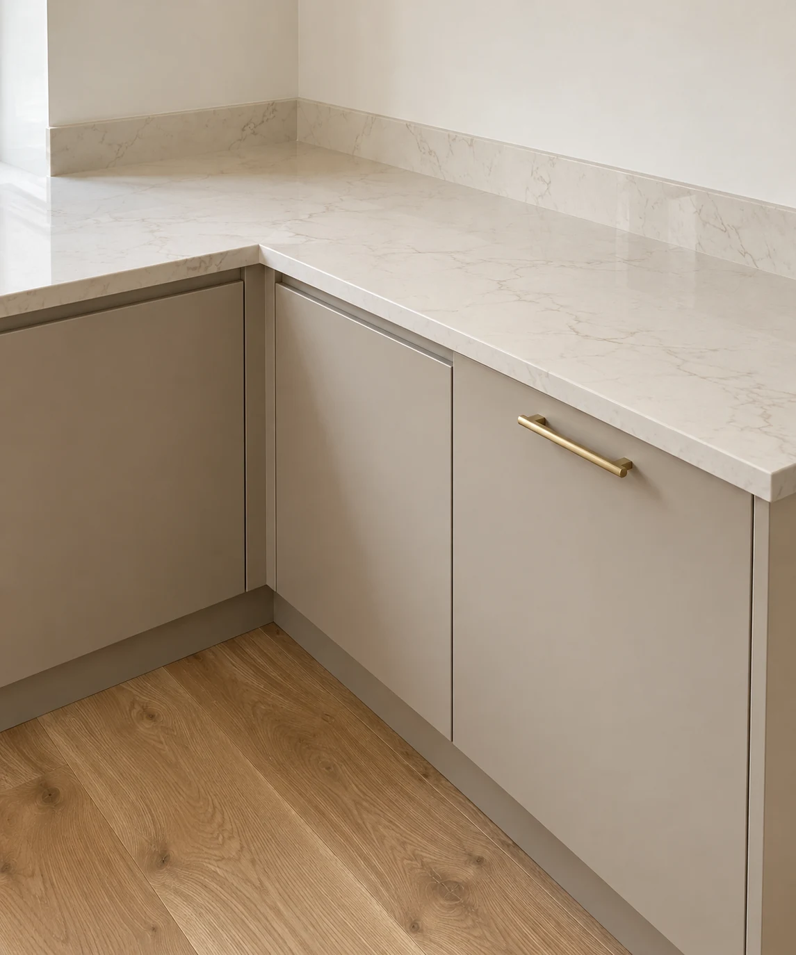 Warm ivory quartz worktop and splashback above greige cabinets and pale oak flooring.